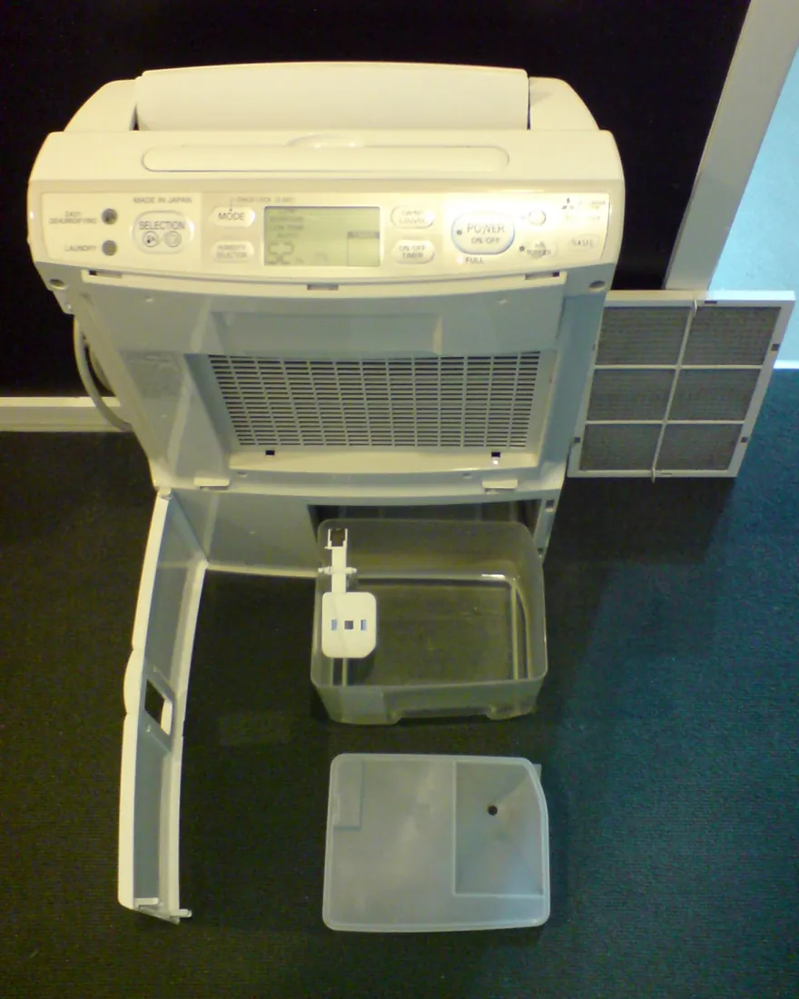 Portable dehumidifier with its water bucket and air filter pulled out beside it
