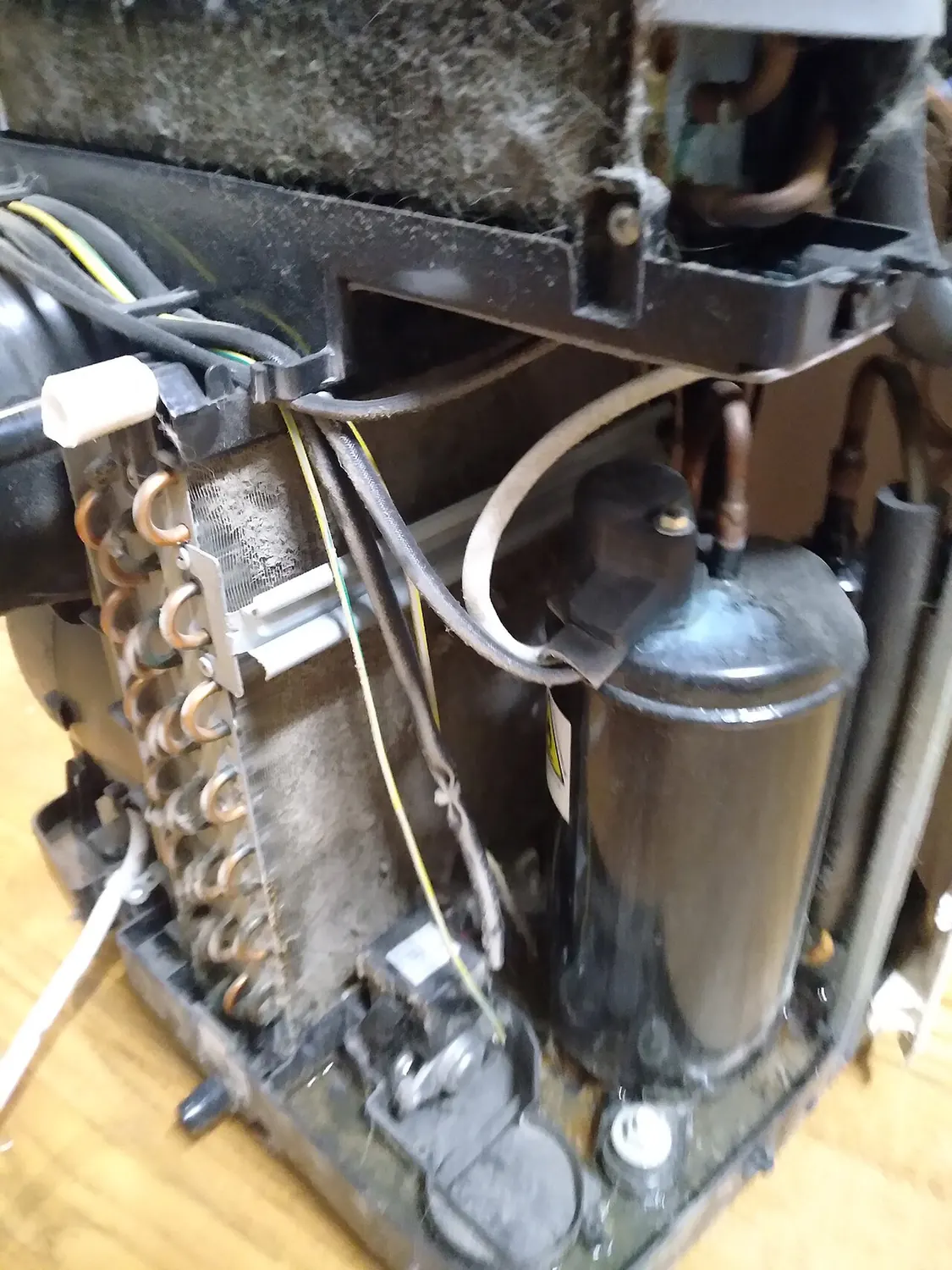 Air conditioner opened up, with gray dust matted on its filter at the top and caked on the copper-tube coil below