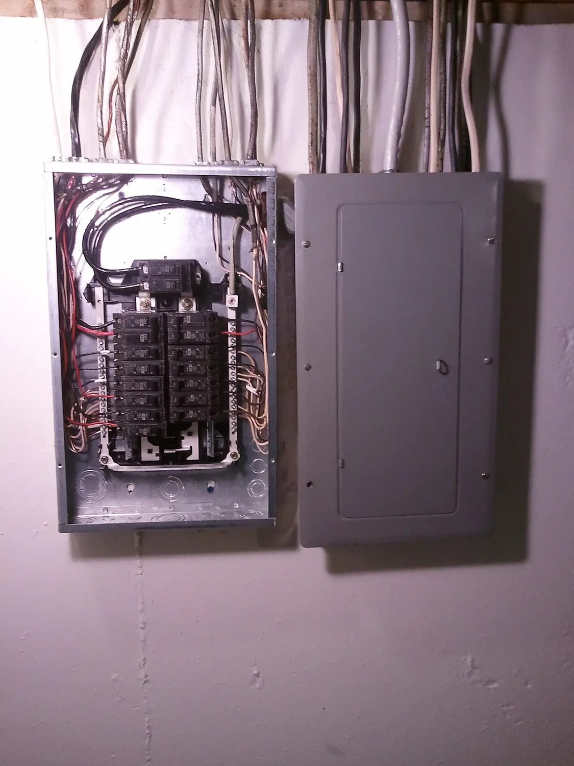 Home electrical panel with labeled circuit breakers next to a subpanel with its cover removed