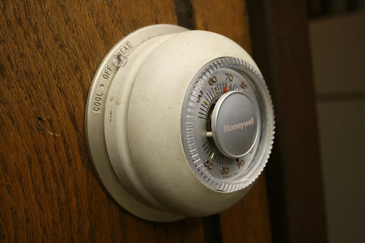 Round Honeywell dial thermostat mounted on a wood-paneled wall