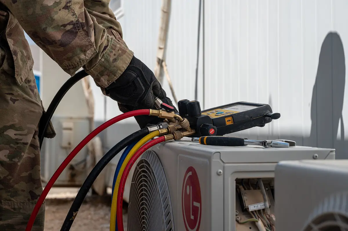 HVAC technician connecting refrigerant gauges to an outdoor unit