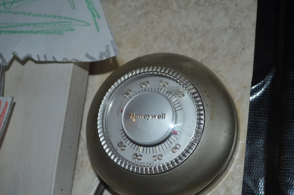 Round Honeywell dial thermostat mounted on a wall right beside a door frame