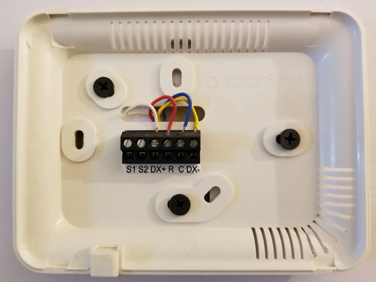 Thermostat base with a six-position terminal block labeled S1, S2, DX+, R, C, DX- and four colored wires connected
