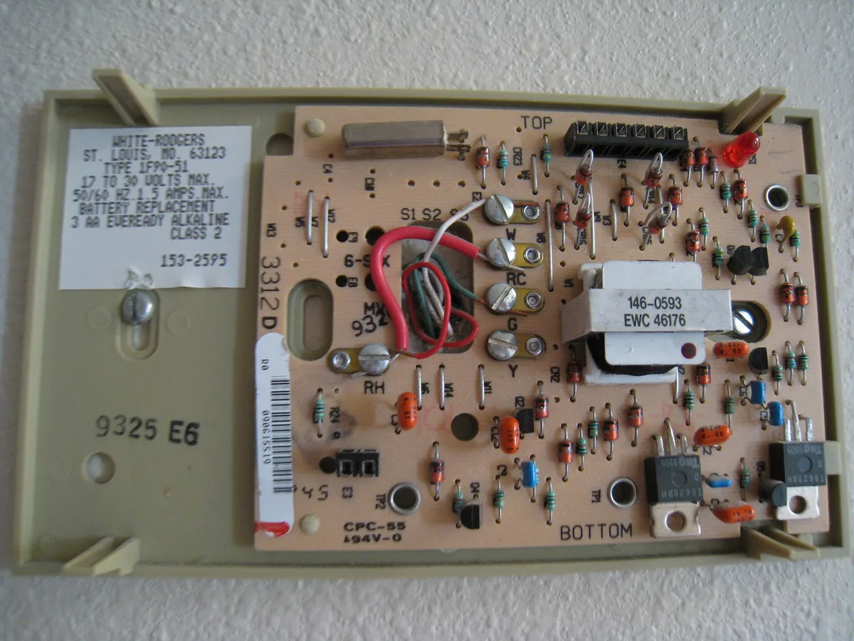 Base of a digital thermostat on a wall with the cover off, showing the circuit board and thermostat wires coming through the wall