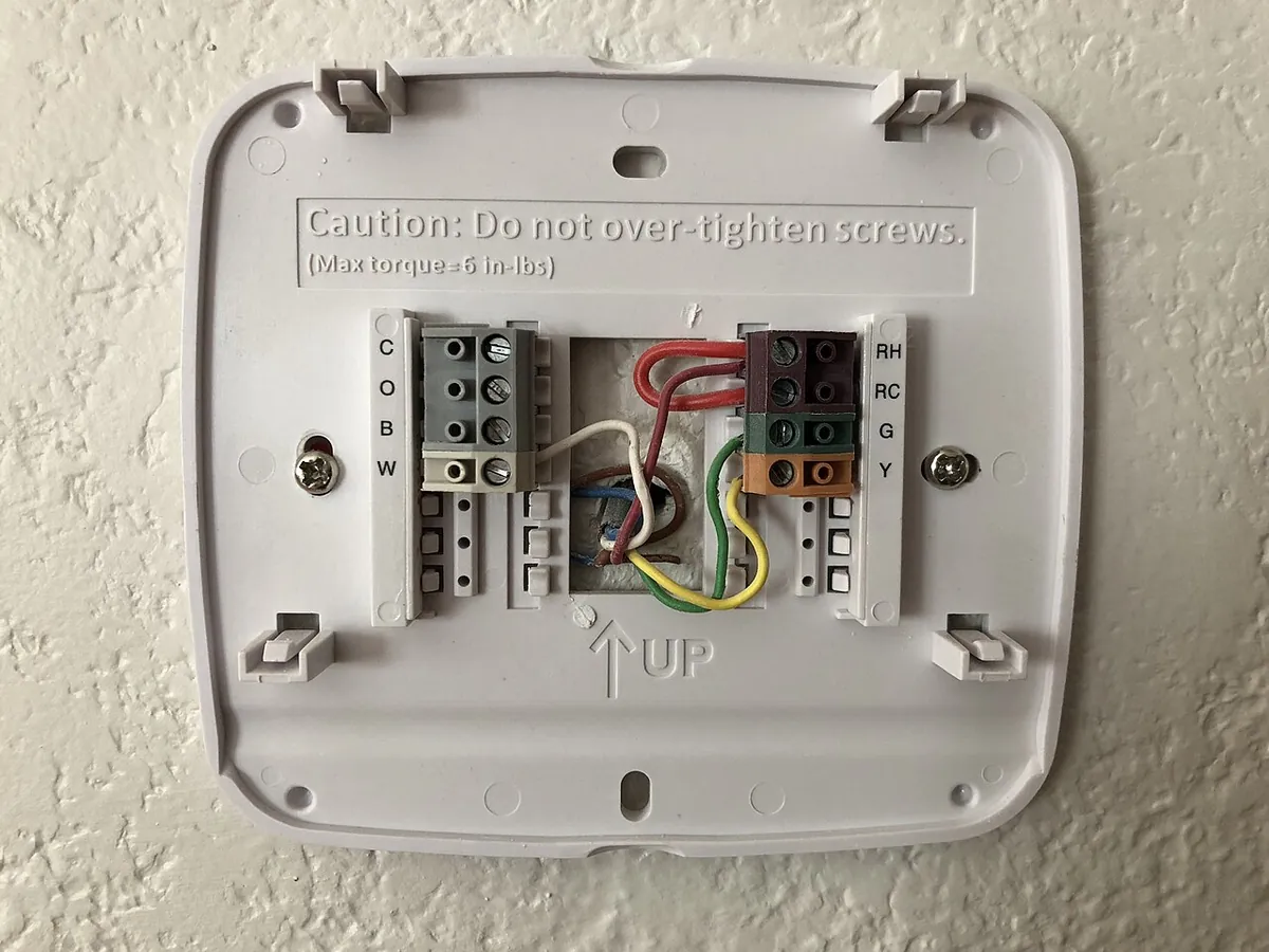 Thermostat wall plate with red, white, green, blue and yellow thermostat wires connected to labeled screw terminals